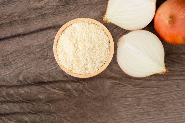 Ground onion or onion powder in wooden bowl and fresh onion with half sliced isolated on wooden table background. Top view. Flat lay